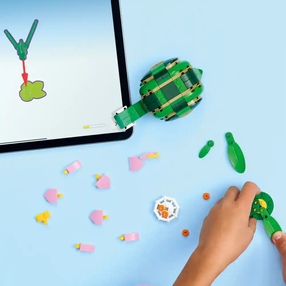 LEGO Creator set 31377 featuring a green buildable sea turtle with articulated flippers, pink water lily flowers with yellow centers, orange spider elements, and green lily pad pieces displayed against a light blue background with product components and a child's hand showing interactive play