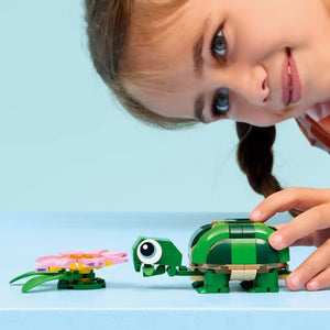 Young child playing with LEGO Creator set 31377 featuring green brick turtle and pink water lily flower against light blue background