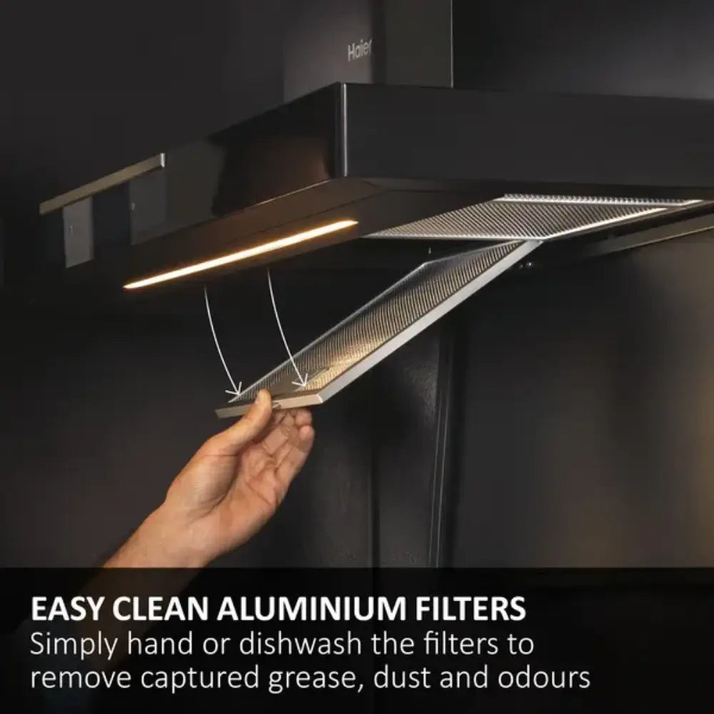 Person holding removable aluminium filter from Haier black cooker hood showing easy-clean mesh design with integrated LED lighting above kitchen counter