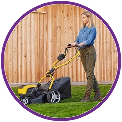 Woman using a lawn mower on grass with a wooden fence in the background
