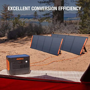 Jackery SolarSage 200W solar panel JS-200D with orange frame and dark grey solar cells set up outdoors next to a Jackery portable power station, connected by orange cable, with lake and mountains visible in background