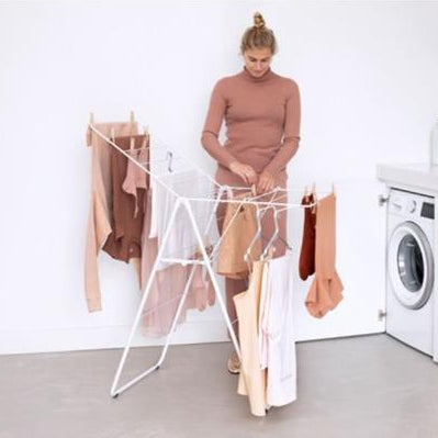 Woman hanging damp laundry on a white metal winged clothes airer with multiple lines in a bright laundry room next to a washing machine