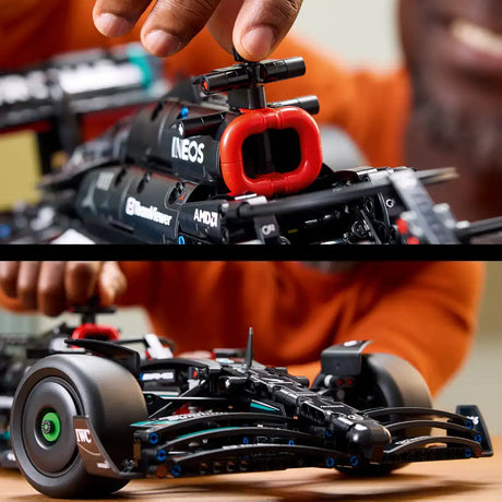 Lego Technic Mercedes-AMG F1 W14 E Performance model 42171 displayed in two views showing detailed black chassis with red intake scoop, cyan accents, realistic gray tires with green hub details, and small replica cameras mounted on top, held by hands against orange background