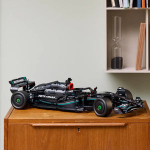 Black Lego Technic Mercedes-AMG F1 W14 E Performance race car model displayed on wooden dresser with white shelving unit in background