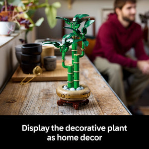 LEGO Lucky Bamboo 10344 decorative plant with green articulated leaves, green segmented bamboo stem with gold bands, and cream and dark red base displayed on wooden table as home decor