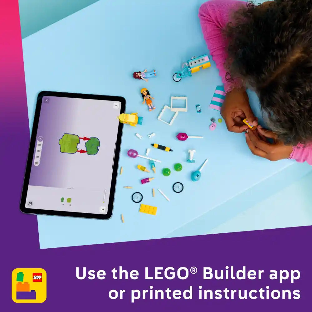 Child in pink shirt building with colorful LEGO pieces on light blue surface next to tablet displaying LEGO Builder app with green brick design, surrounded by scattered yellow, pink, and turquoise LEGO elements, minifigures, and accessories for Ice Cream and Balloon Stand set 42692