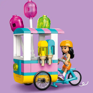 LEGO Friends ice cream and balloon stand set 42692 featuring a colorful turquoise pink and yellow modular cart with striped awning, yellow and blue ice cream dispensers, three translucent balloon toppers in magenta lime and pink, and a mini doll figure with orange helmet on a turquoise bicycle against a purple background