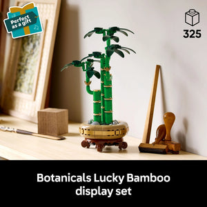 LEGO Botanicals Lucky Bamboo display set featuring green buildable bamboo stalks with leaves in a tan and brown decorative pot, accompanied by wooden plant care accessories, displayed on a shelf with "perfect as a gift" badge and 325 piece count indicator