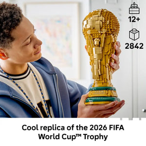 Young person holding a gold and green LEGO FIFA World Cup Trophy replica set containing 2842 pieces, suitable for ages 12 and up, displayed against a bright indoor background