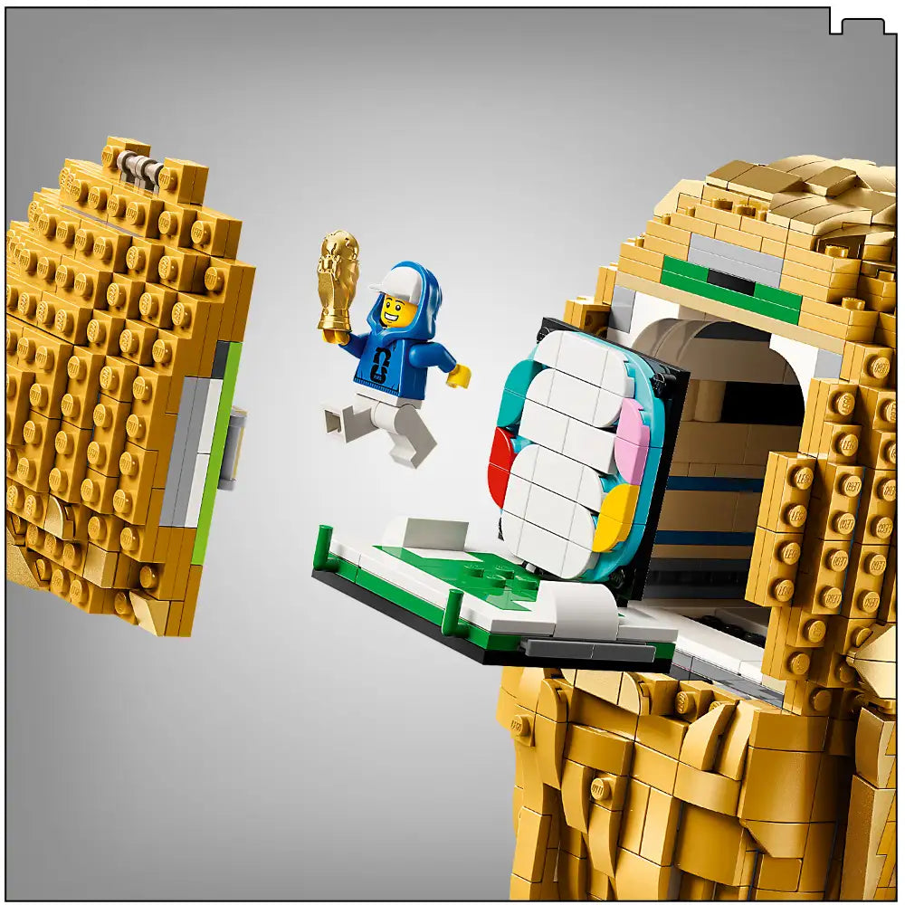 LEGO FIFA World Cup Official Trophy set 43020 featuring golden brick structures with a blue minifigure holding the gold trophy, colorful turntable base with white, green, pink and yellow elements, displayed against a grey background