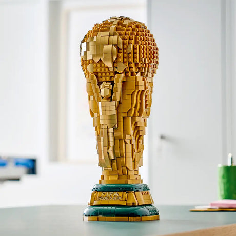 LEGO FIFA World Cup Trophy set 43020 in gold and teal colors displayed on white desk with green cup and papers in background