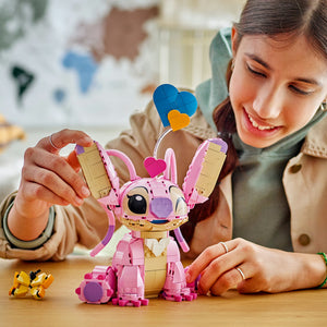 Young child playing with LEGO Angel 43257 set, a pink and tan buildable character figure with articulated arms and legs, colorful heart-shaped accessories in blue, yellow and purple, displayed on wooden table during playtime