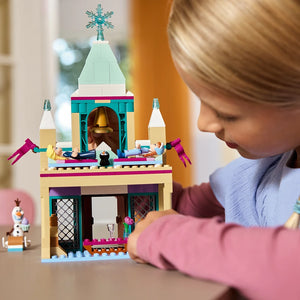 Child playing with LEGO Arendelle Castle set 43265 featuring turquoise and cream colored building with golden bell tower, snowflake topper, and Frozen character minifigures on wooden surface
