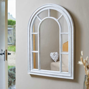 Silvergris arched window-style wall mirror with white frame and geometric pane divisions, displayed in a bright interior setting near open garden doors with dried pampas grass decoration