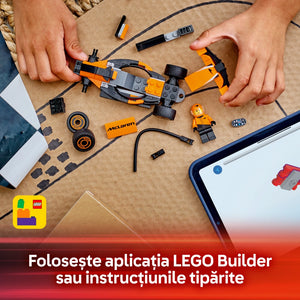 Child's hands assembling an orange and black LEGO McLaren Formula 1 race car set on a beige surface, with instruction manual, minifigure driver, wheels, and building pieces visible, alongside a smartphone displaying LEGO Builder app instructions