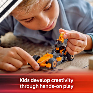 Child playing with orange and black LEGO F1 McLaren race car and driver figure on ground, demonstrating hands-on creative play with construction toys