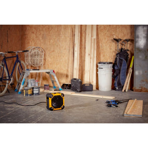 Dimplex Rugged 3KW workshop electric fan heater in yellow and black displayed on concrete floor in industrial garage setting surrounded by tools, bicycles, and building materials