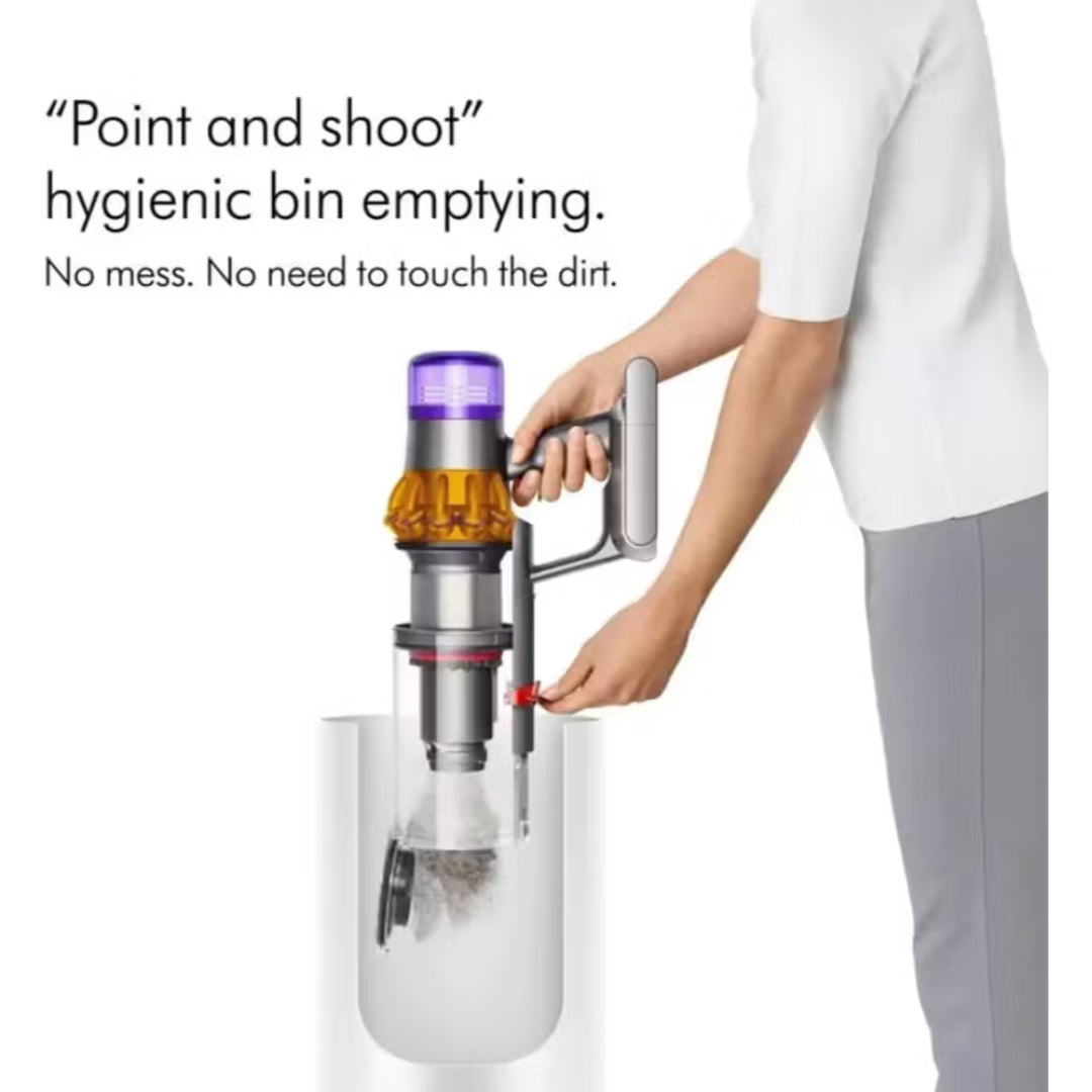 Person demonstrating hygienic bin emptying feature of Dyson V15 Detect vacuum with point and shoot mechanism, showing stainless steel dustbin with purple top cap and red release button, dirt visible in collection chamber below