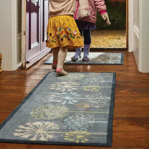 Hug Rug runner mat with nature tree design in grey blue and yellow displayed in home hallway with wooden flooring, child wearing yellow skirt visible in doorway