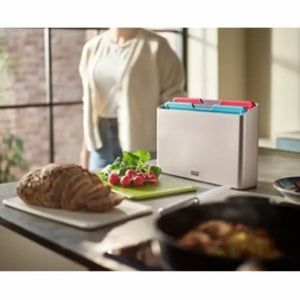 Joseph Joseph Folio Icon 4 piece chopping board set in white with colorful tabs including red, blue and green, displayed on a kitchen counter with bread, radishes and cooking pan