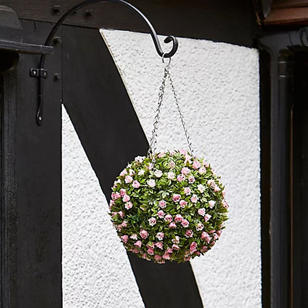 Hanging topiary ball with pink and white flowers suspended from black metal bracket against white textured wall