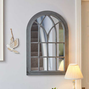 Arched Victorian-style mirror with slate gray wooden frame and geometric pane design, mounted on white wall next to decorative gold leaf ornament and cream lamp shade