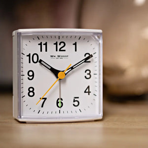 White square alarm clock by Wm. Widdop with black numerals, black hour and minute hands, yellow second hand, yellow center circle, and sweep movement mechanism on wooden surface