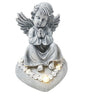Solar-powered stone angel grave ornament with praying hands, decorative white flowers at base, wings spread, suitable for cemetery memorial display