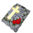 Gray stone memorial grave ornament with illuminated yellow cross, red roses, green ivy leaves, and engraved text reading "You may be out of sight but never out of our hearts"