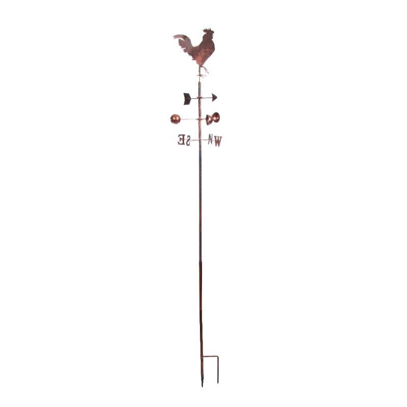 Rustic copper rooster weather vane with directional cardinal points (N, S, E, W) mounted on tall metal pole with ground stake