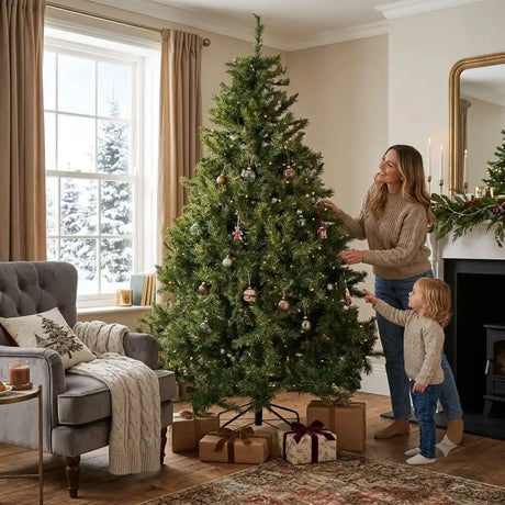 Woman and young child decorating a 8ft Colorado Fir Christmas tree with gold and burgundy ornaments in a bright living room with cream walls, beige curtains, fireplace, wrapped presents at base, and snowy trees visible through large window