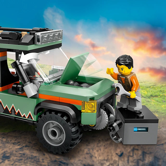 LEGO off-road 4x4 mountain truck set 60447 featuring a green and orange vehicle with opening cargo bed, black-haired minifigure in orange jacket, gray storage box, and dramatic mountain landscape background with blue sky and sunset clouds