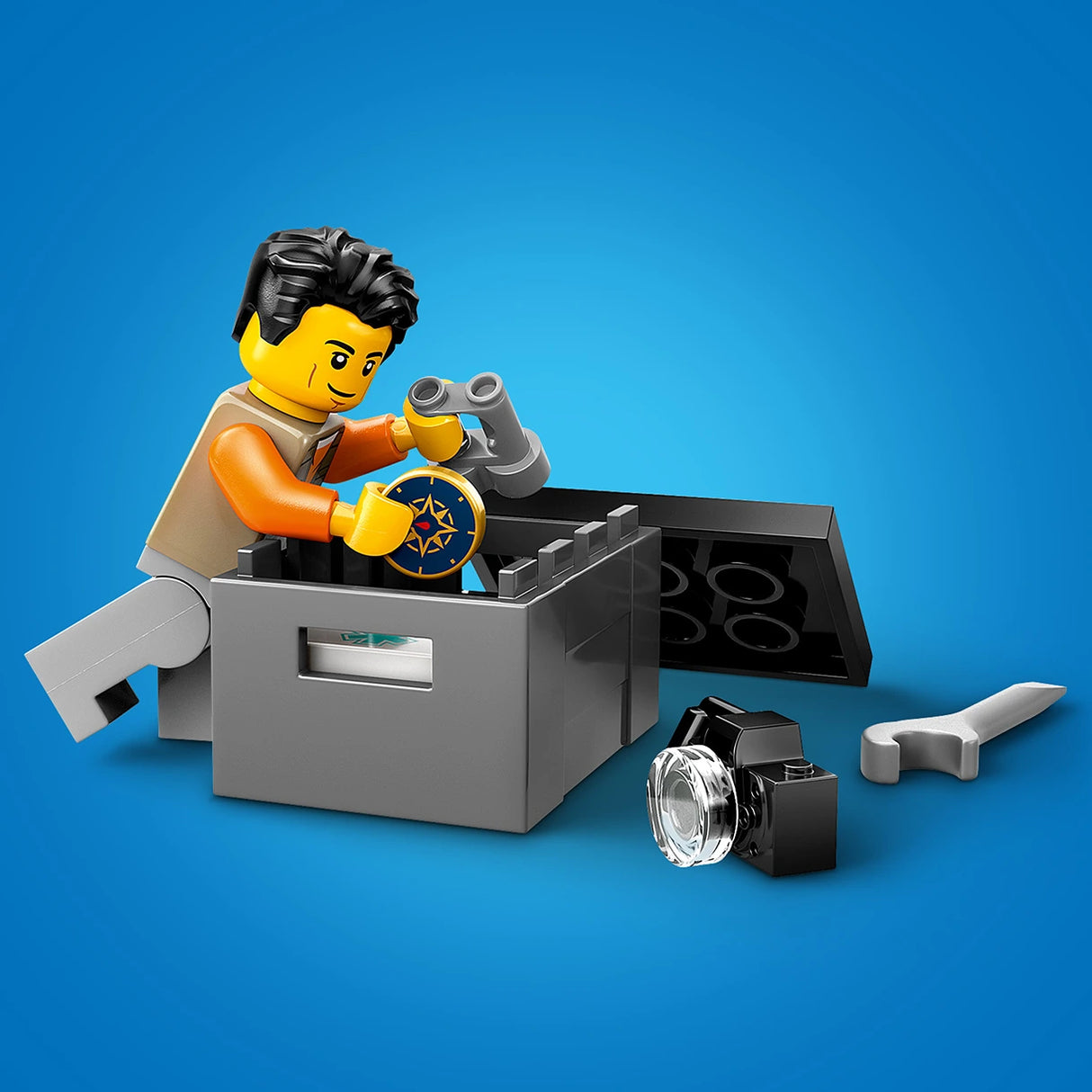 LEGO minifigure with black hair and yellow face wearing orange torso sitting in gray command station with binoculars and star-emblazoned badge, accompanied by black camera with lens and white wrench on blue background