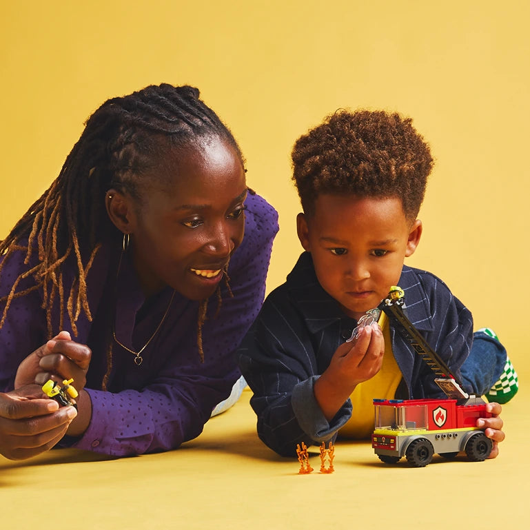 Woman and young child playing with LEGO Fire Ladder Truck set 60463 against yellow background, holding minifigures and red and cream colored fire truck model