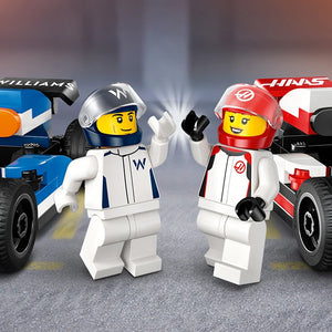 Two LEGO minifigures in racing suits stand between a blue Williams F1 race car and a red Haas F1 race car on an asphalt track, with the minifigures wearing matching helmets and waving