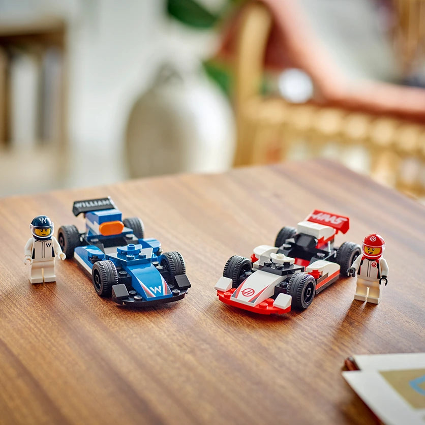 LEGO F1 racing set featuring blue Williams and red Haas Formula 1 cars with minifigure drivers displayed on wooden table in home setting