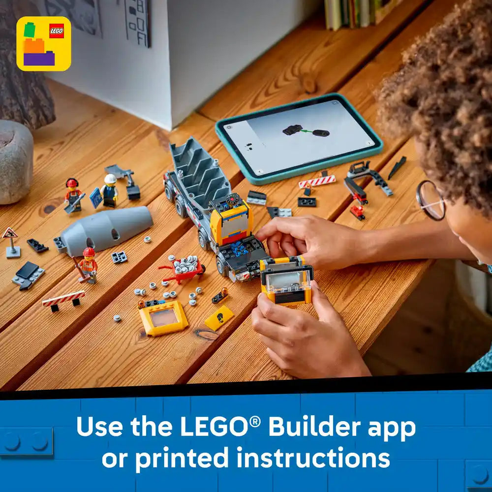 Child's hands assembling a yellow and blue LEGO cement mixer truck on a wooden table with instruction manual displayed on tablet, surrounded by LEGO bricks, minifigures and construction accessories