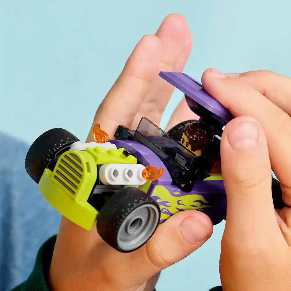 Child's hand holding a LEGO Hot Rod 60485 set featuring a neon yellow and purple race car with black wheels and orange flame details against a blue sky background