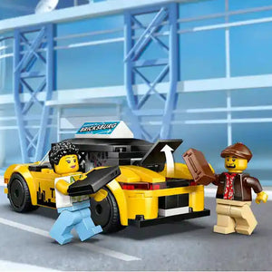 LEGO yellow taxi set 60487 featuring bright yellow car with black details, two minifigures in casual clothing, and modern blue glass building background