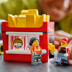 LEGO food truck toy set featuring red and yellow French fries stand with two minifigures in orange and red uniforms, yellow fries accessory, and number 5 coin detail on grey surface with blurred background