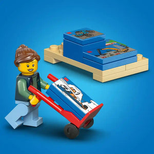LEGO minifigure with brown hair pushing a red and blue toy van loaded with blue LEGO instruction boxes on a tan display shelf against a bright blue background