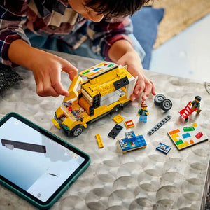 Child's hands holding a bright yellow LEGO van set with construction worker minifigures, building blocks, and instruction manual displayed on a textured surface next to a smartphone