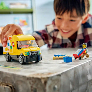 Child playing with LEGO City yellow and white van set featuring a minifigure, blue cargo box, and red cart on a grey surface with blurred background