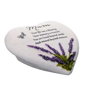 White heart-shaped stone memorial with purple lavender flowers and green stems, featuring handwritten "Mum" at top and engraved text reading "Your life was a blessing, Your memory a treasure, You are loved beyond words, And missed beyond measure," with decorative butterfly detail