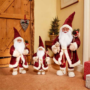 Three decorative Santa Gnome figures in burgundy and cream displaying traditional Christmas decor with tall pointed hats, white beards, and festive clothing arranged on carpeted floor near wooden door