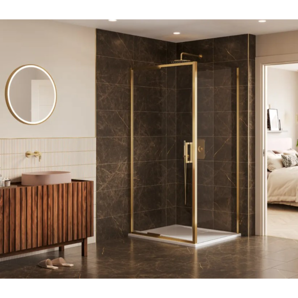 Modern corner shower enclosure with brushed brass frame and clear glass panels featuring an infold door, installed in a luxury bathroom with dark brown marble-effect wall and floor tiles, wooden slatted vanity unit with pink basin, round backlit mirror, and cream walls with vertical ribbed tiles