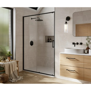 Modern bathroom featuring a Merlyn 6 Series black framed sliding shower door with frosted glass panels, chrome fixtures and rainfall showerhead, light wood vanity with white countertop and vessel sink, wall-mounted black faucet, pendant lighting, beige tile walls and flooring, green window with plants, and contemporary Scandinavian styling