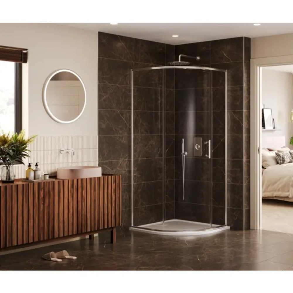 Modern bathroom featuring a curved quadrant shower enclosure with chrome frame and clear glass doors, set against dark brown marble-effect wall tiles, white shower tray, wooden slatted vanity unit with pink vessel sink, round backlit mirror, and matching dark marble floor tiles
