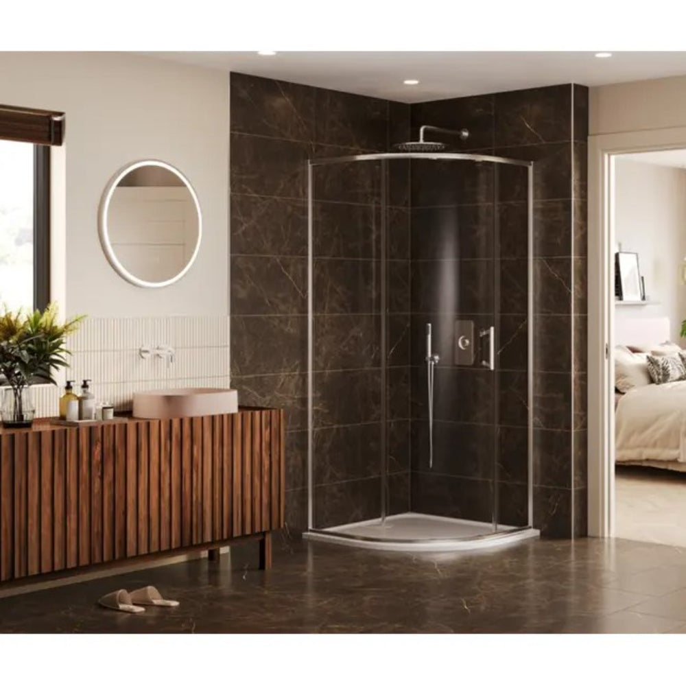 Modern quadrant shower enclosure with curved glass doors and chrome frame, featuring a white shower tray, rainfall showerhead, and handheld shower attachment, installed in a contemporary bathroom with dark brown marble-effect wall tiles, matching floor tiles, wooden slatted vanity unit with pink basin, round LED backlit mirror, and view into adjoining bedroom