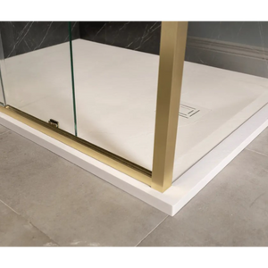 Modern Merlyn 6 Series sleek sliding shower door with brushed brass frame and clear glass panel installed in white acrylic shower tray with dark marble-effect wall panels in contemporary bathroom setting